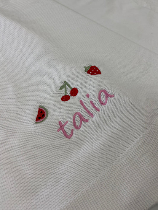Embroidered name 'Talia' with strawberry and watermelon, cherries and strawberry designs on a white blanket background